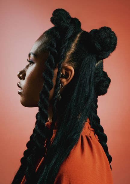 Edgy young black woman with trendy afro hairstyle against an orange studio background. Profile of a confident, serious and stylish african american female with bold personality and cool attitude